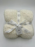 A folded cream-colored fluffy throw blanket tied with a white ribbon printed with the K Squared logo, on a light gray background.