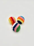 Three small crocheted striped balls in rainbow colors, arranged on a plain light gray background.