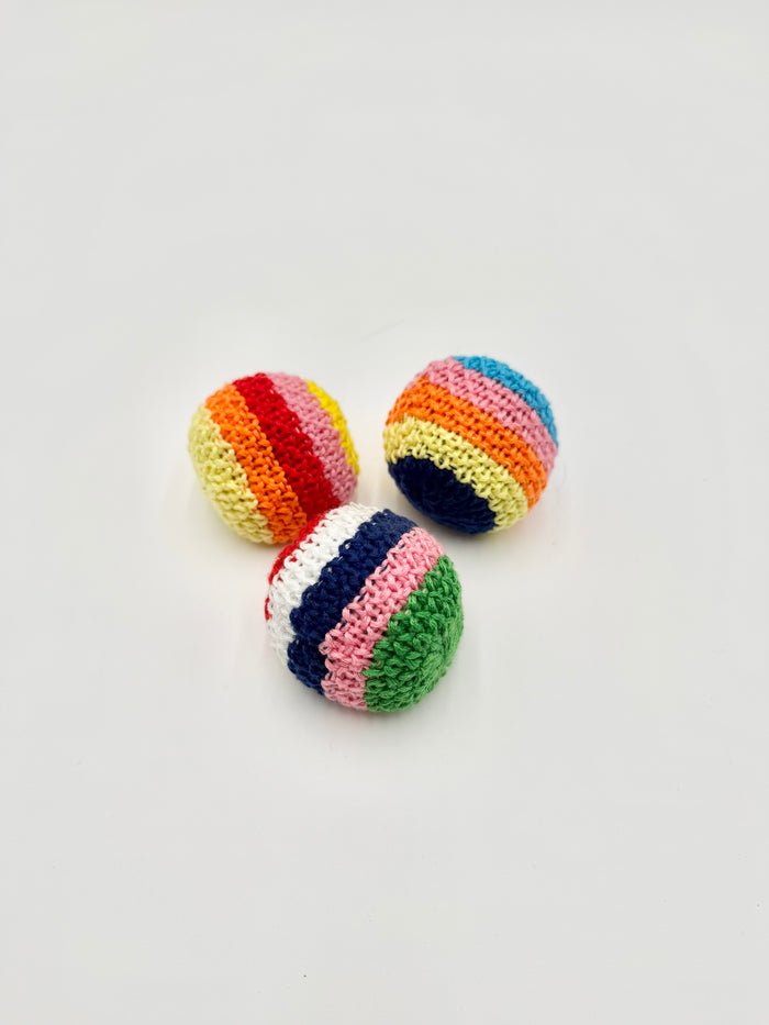 Three small crocheted striped balls in rainbow colors, arranged on a plain light gray background.