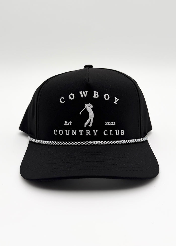A black baseball cap with white embroidered text reading 'COWBOY COUNTRY CLUB' and a golfer silhouette on the front, plus a silver chain detail across the brim, shown on a light gray background.