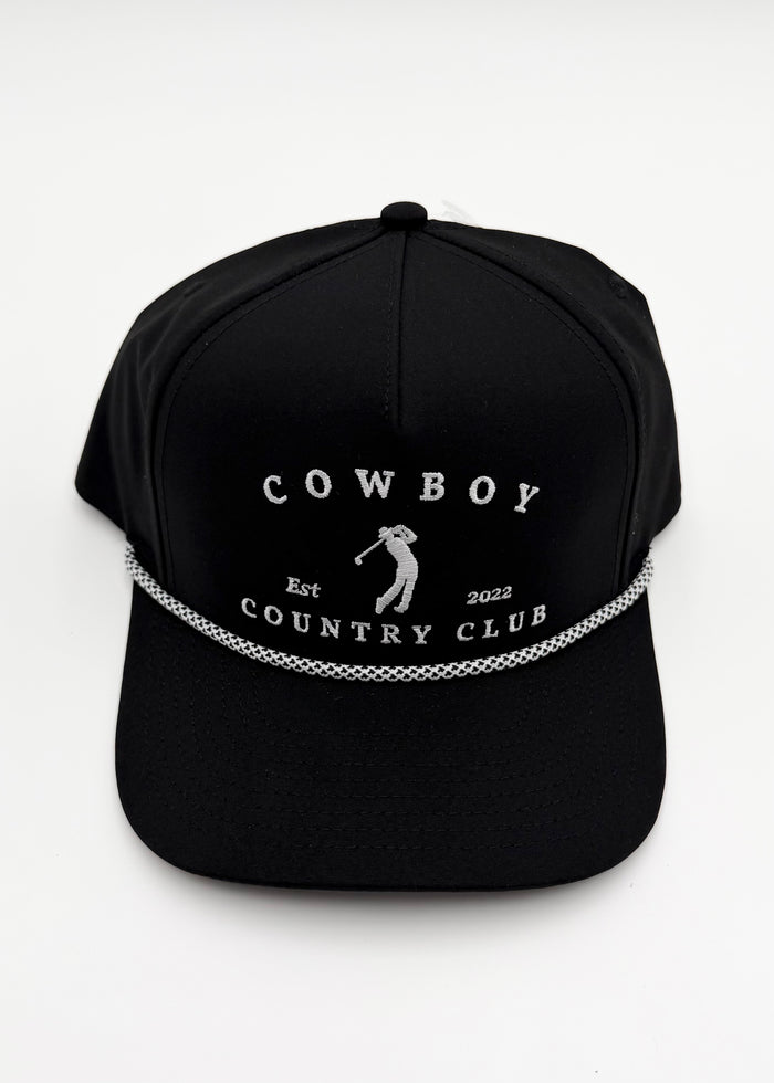 A black baseball cap with white embroidered text reading 'COWBOY COUNTRY CLUB' and a small golfer silhouette, plus a decorative white chain-like line across the front, shown on a plain light background.