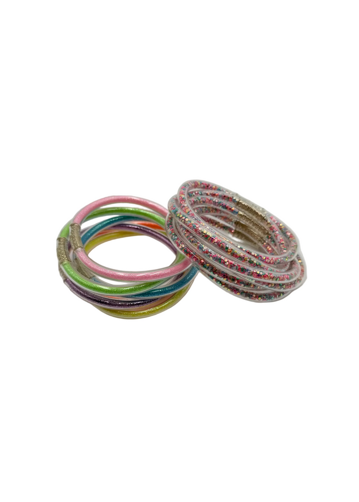 Two stacks of thin bangles or rings on a plain light gray background. One stack contains multicolored bands, and the other appears to be silver-toned bands with small multicolored speckles.