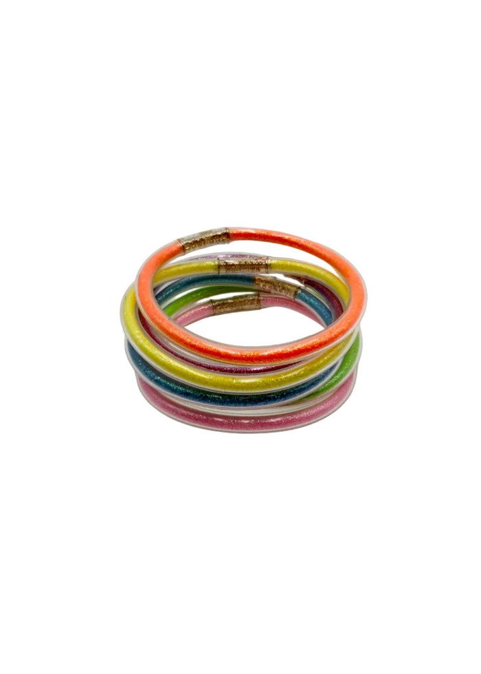 A stack of six thin elastic bangles in assorted bright colors, including orange, green, yellow, blue, pink, and white, with small gold-toned metal connectors, photographed on a plain light background.