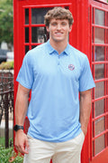 A smiling young man wearing a light blue short-sleeve polo shirt with a circular 'SIP' monogram logo on the left chest, standing in front of a bright red telephone booth.