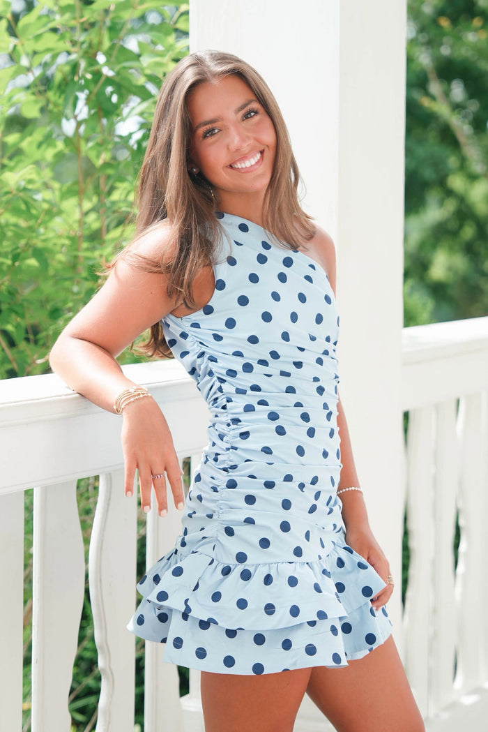 Woman wearing a blue polka dot dress on a white railing with greenery in the background