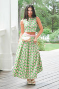 Woman in a green floral dress standing on a wooden deck with trees in the background