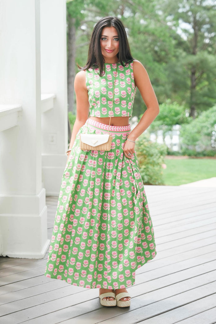 Woman in a green floral dress standing on a wooden deck with trees in the background