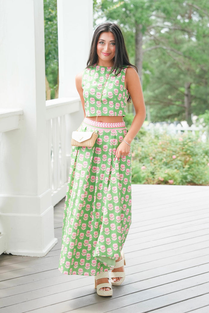 Woman in a green floral dress standing on a wooden deck with a white railing.