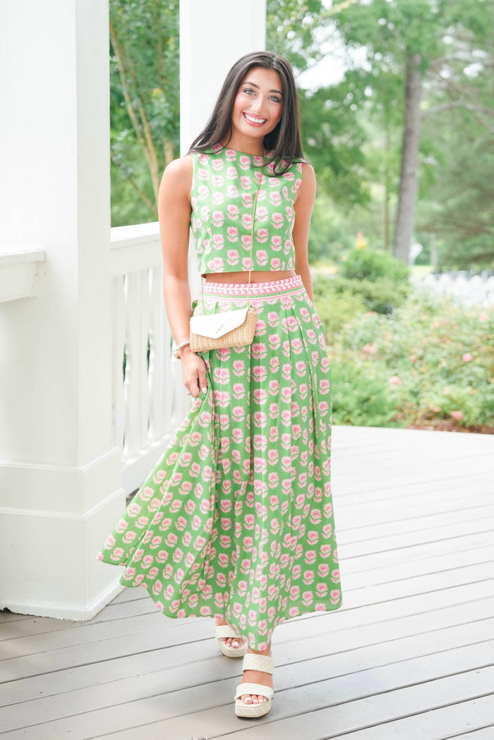 Woman in a green floral dress standing on a wooden deck with a garden background