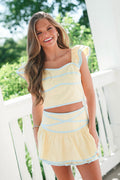 Woman wearing a yellow and blue striped dress on a white railing with greenery in the background