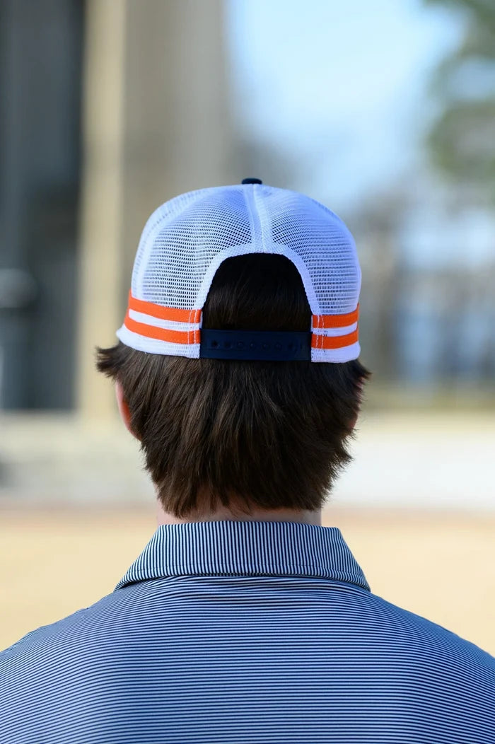 A man viewed from behind wearing a white mesh back trucker cap with orange stripes and a navy adjustable strap, paired with a blue striped polo shirt in an outdoor setting.
