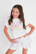 Young girl wearing a white t-shirt with a colorful butterfly design and patterned shorts on a white background