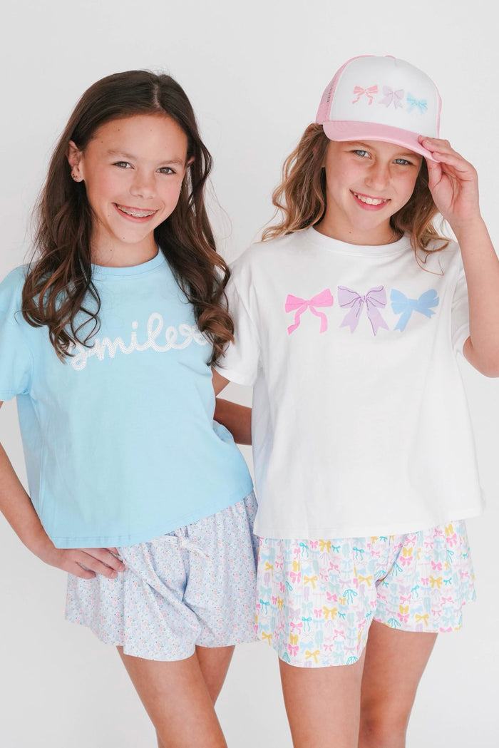 Two young girls wearing matching outfits with colorful bows on a white background