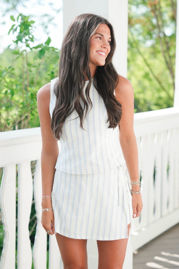 Woman wearing a light blue striped dress on a white railing with greenery in the background