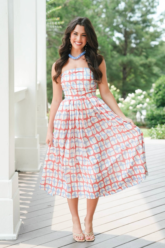 Woman in a patterned dress standing on a wooden deck with greenery in the background