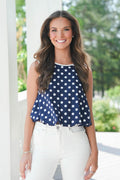 Woman wearing a navy blue top with white polka dots and white pants outdoors.