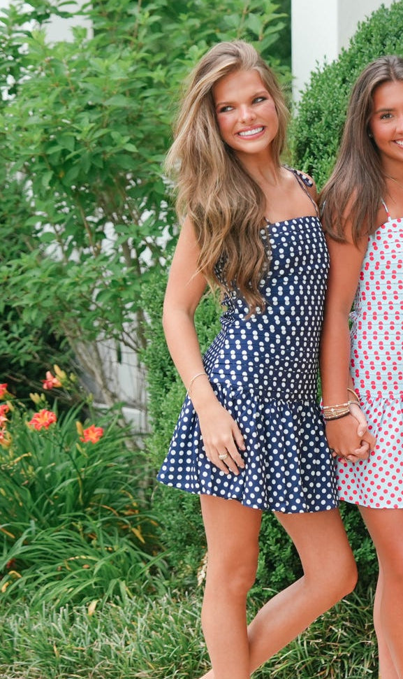 Two women wearing polka dot dresses standing outdoors with greenery in the background