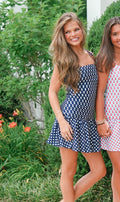 Two women wearing polka dot dresses standing outdoors with greenery in the background