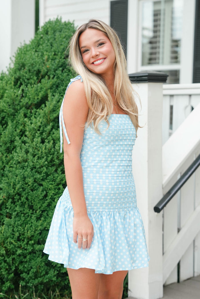 Woman wearing a light blue dress standing outdoors next to a white railing.