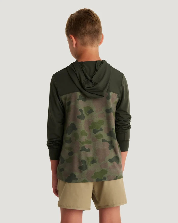 Boy wearing a green and camouflage hoodie and tan shorts with flip flops standing in front of a white background.
