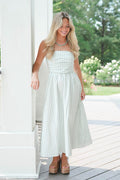 Woman in a white strapless dress standing on a porch with greenery in the background