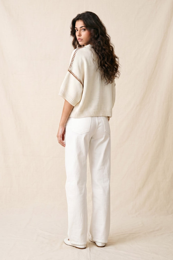 Woman wearing a cream sweater and white pants against a beige background