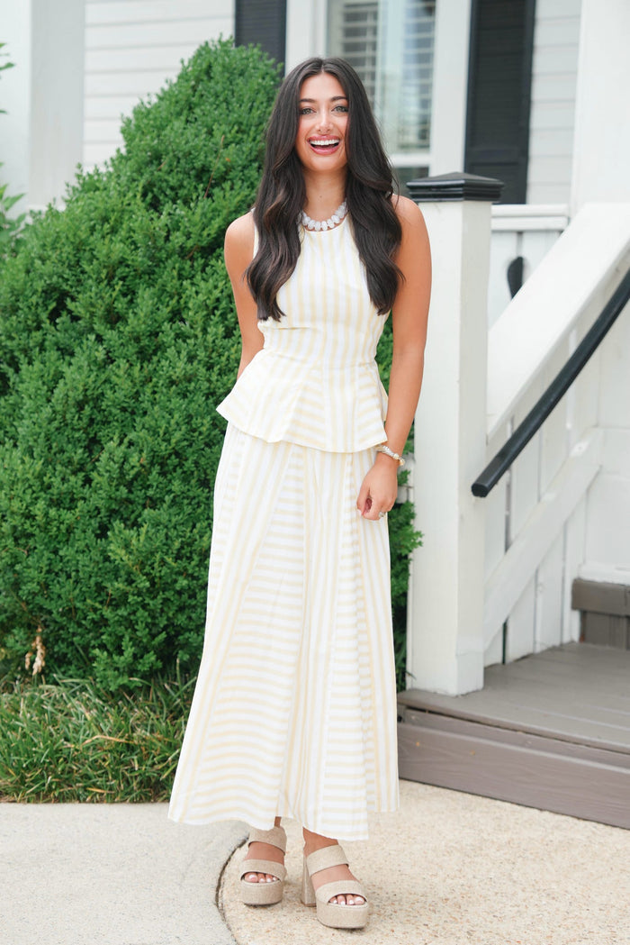 Woman in a white dress standing on a porch with greenery in the background