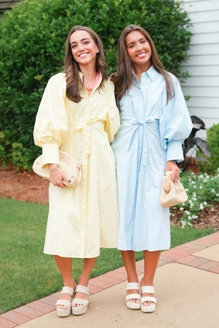 Two women wearing pastel-colored robes standing outdoors on a sidewalk.