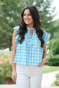 Woman wearing a blue checkered top outdoors with greenery in the background