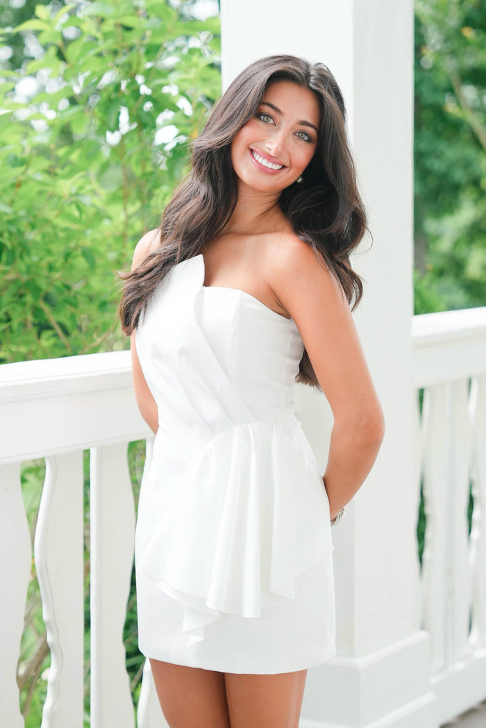 Woman in a white dress standing on a white railing with greenery in the background