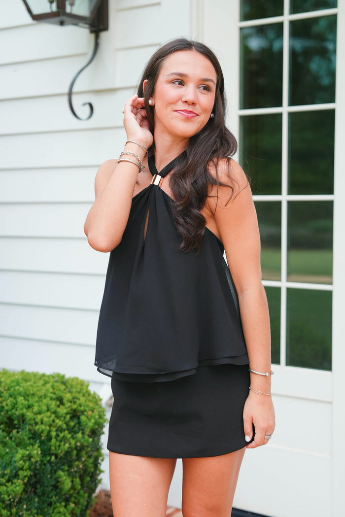 Woman wearing a black dress standing in front of a white house.
