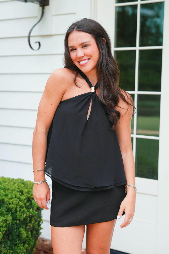 Woman wearing a black dress standing outside a house.