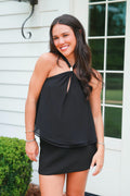 Woman wearing a black dress standing outside a house.