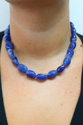 A close-up of a person wearing a chunky cobalt blue beaded necklace with polished oval beads, paired with a black top.