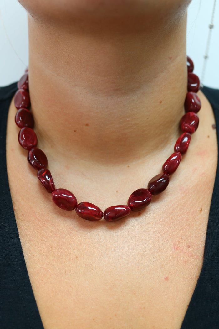 A close-up of a person's neck and chest wearing a dark red beaded necklace with polished oval beads.