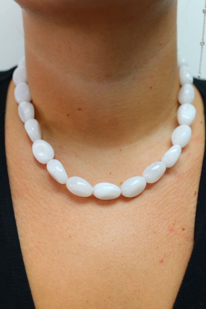 A close-up of a person wearing a double-strand white beaded necklace with smooth, rounded teardrop-shaped beads over a black top.