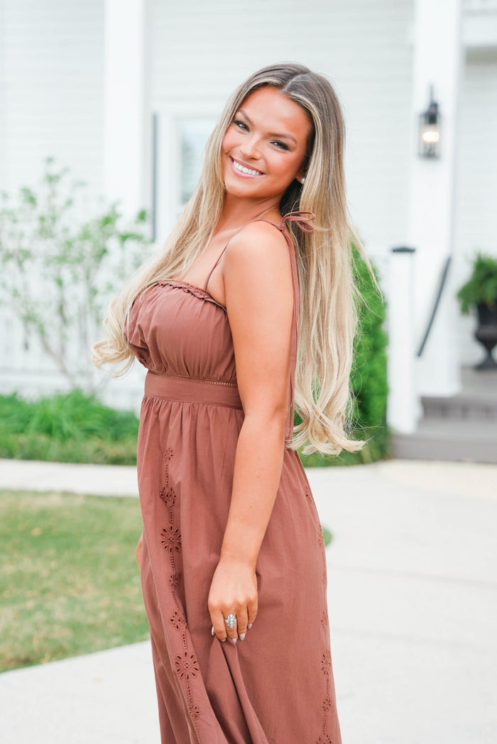 Woman in a brown dress standing outdoors with a blurred background