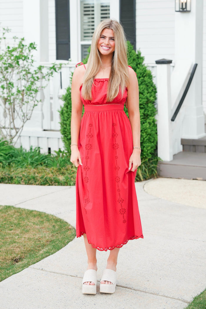 Woman in a red dress standing on a sidewalk with a white house in the background
