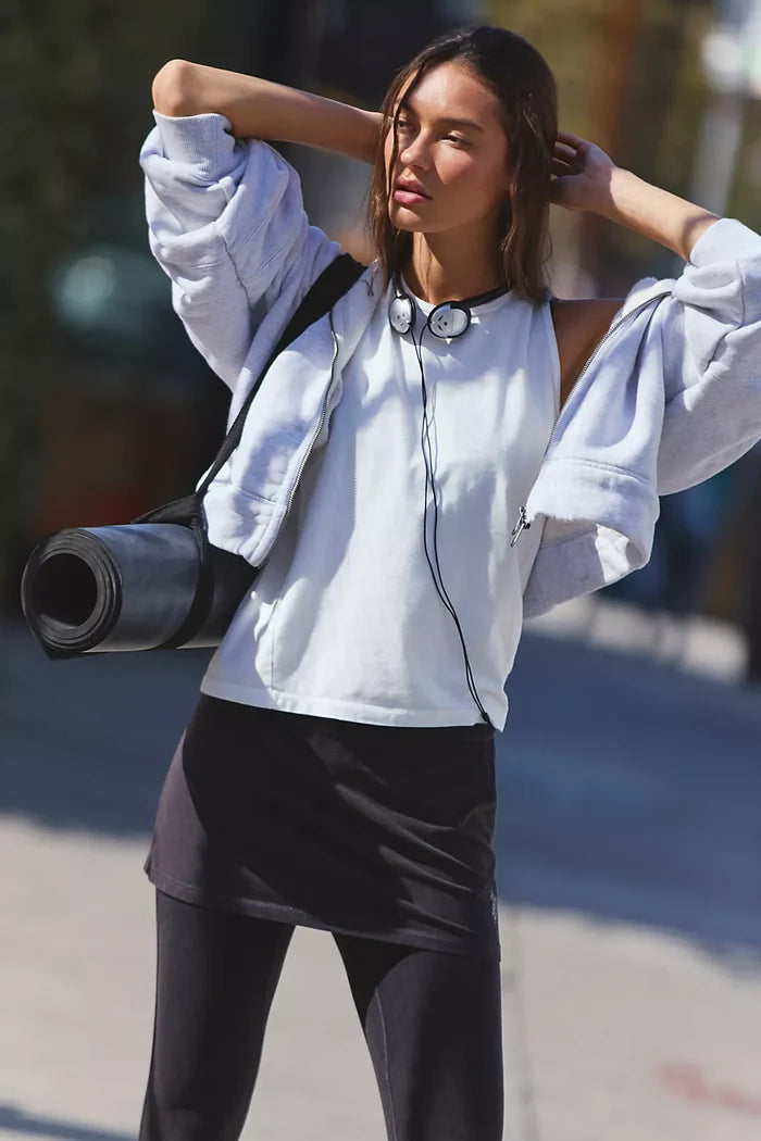 Person wearing a light gray sweatshirt and black leggings, holding a yoga mat.