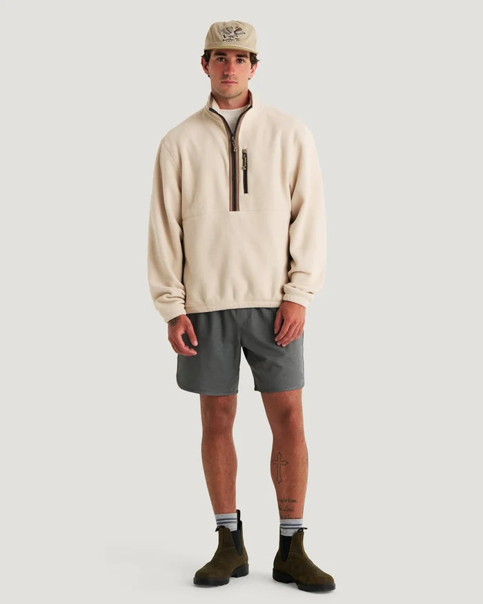 Man wearing a beige pullover, gray shorts, and brown boots on a light gray background