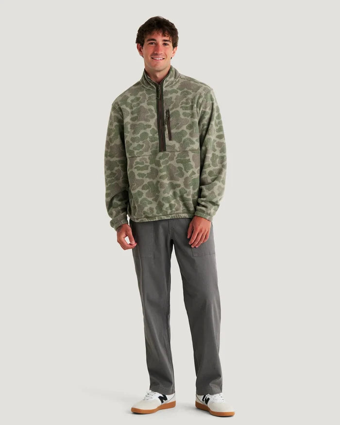 Man wearing a camouflage pullover and gray pants on a white background