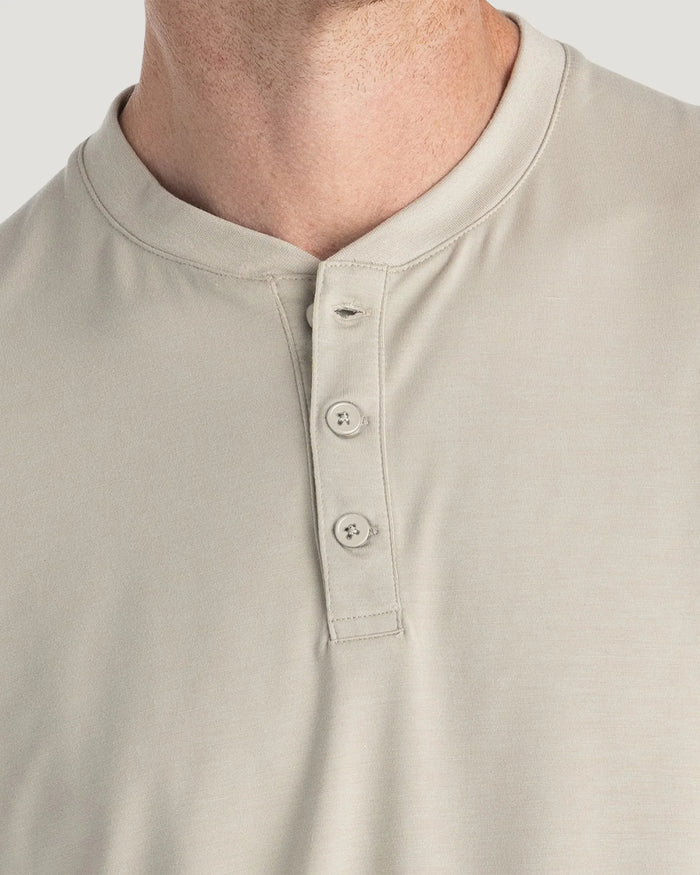 Close-up of a man wearing a light beige henley shirt, showing the collar, three-button placket, and fabric texture.