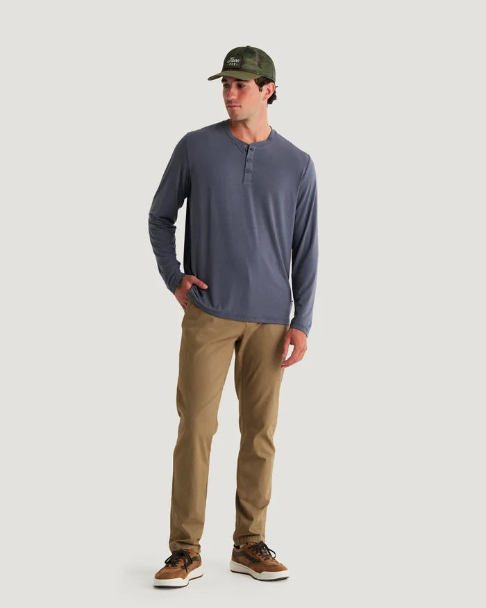Man wearing a blue long-sleeve shirt, brown pants, and a green cap on a white background