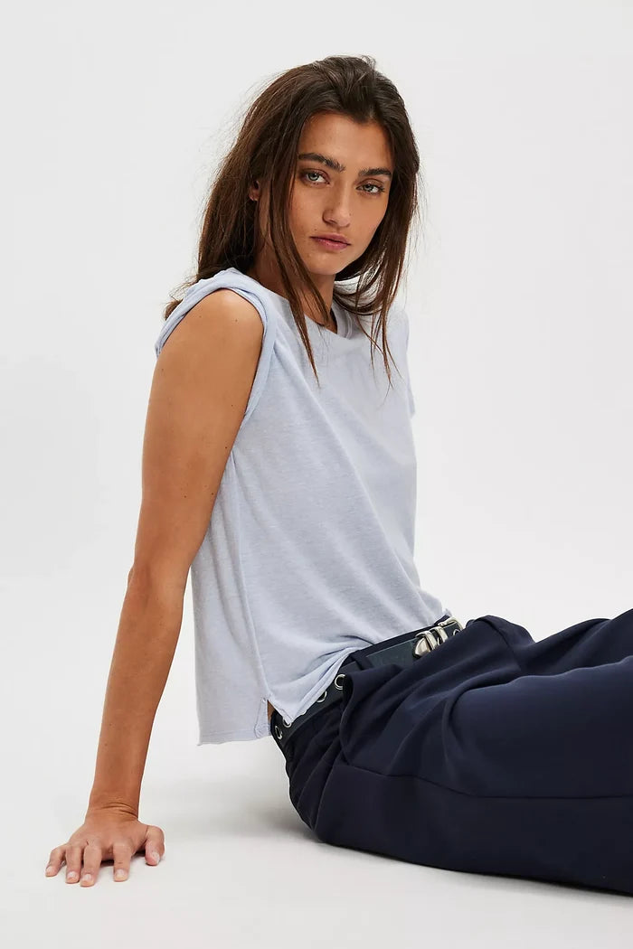 Woman wearing a light blue sleeveless top and dark pants sitting on a white surface.