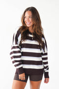 A woman modeling a brown and white horizontally striped quarter-zip sweatshirt with ribbed cuffs and hem, paired with dark brown shorts, against a plain white background.