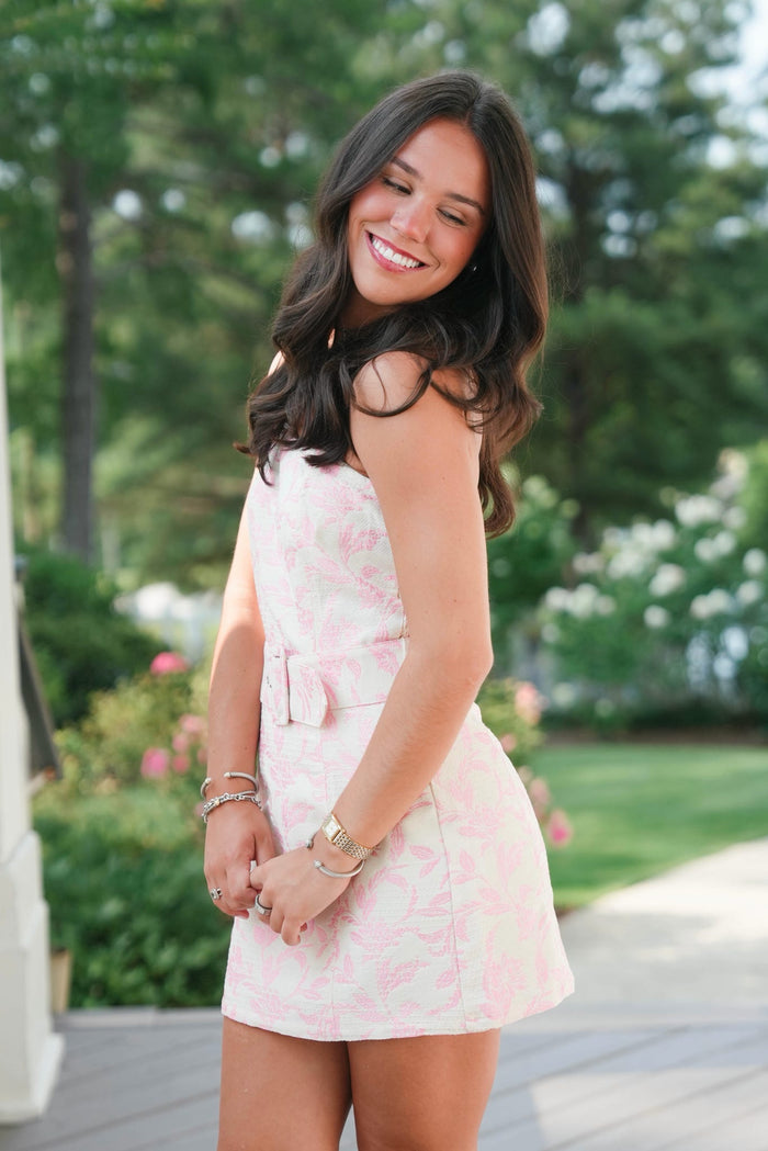 Woman in a pink floral dress standing outdoors with greenery in the background