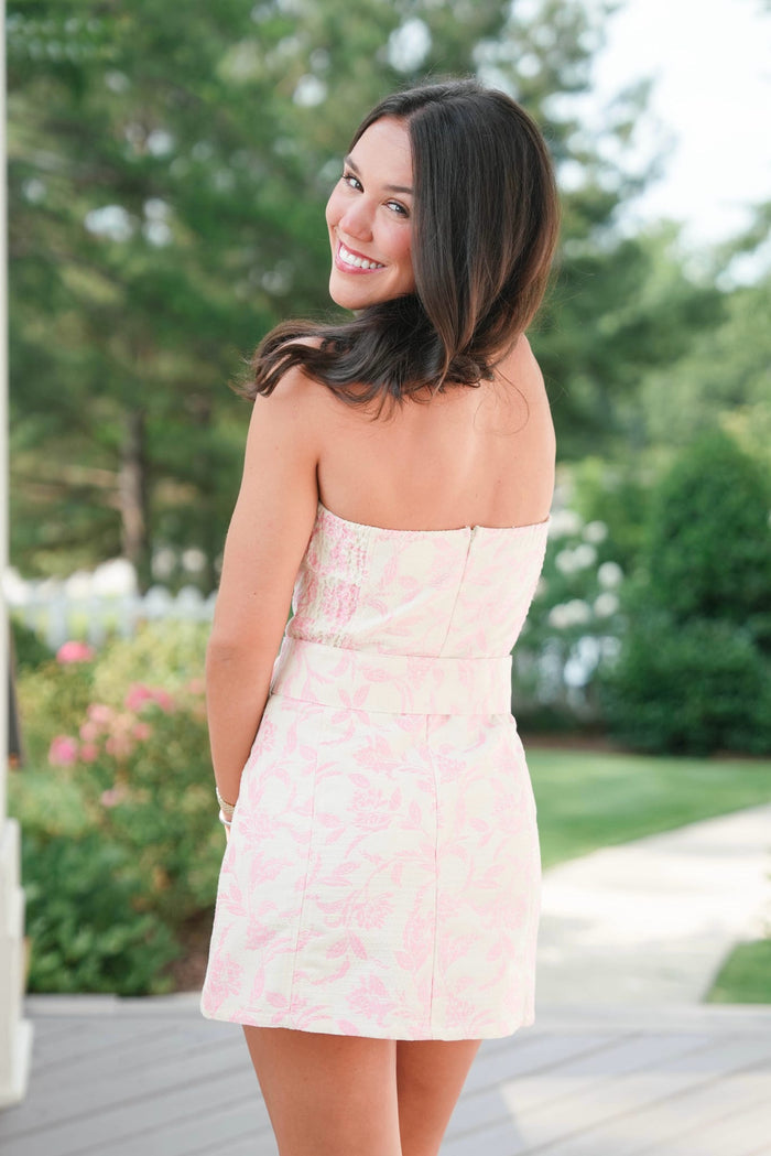 Woman in a strapless dress standing outdoors with greenery in the background