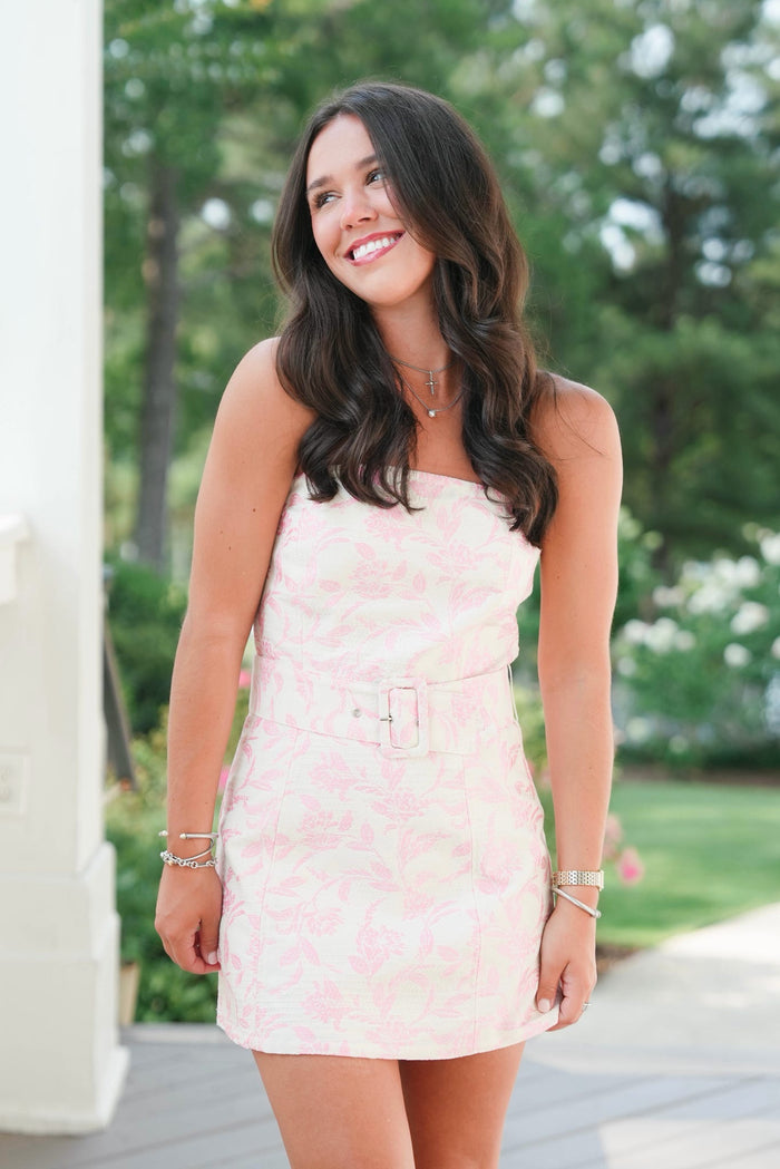Woman in a pink dress standing outdoors with trees in the background