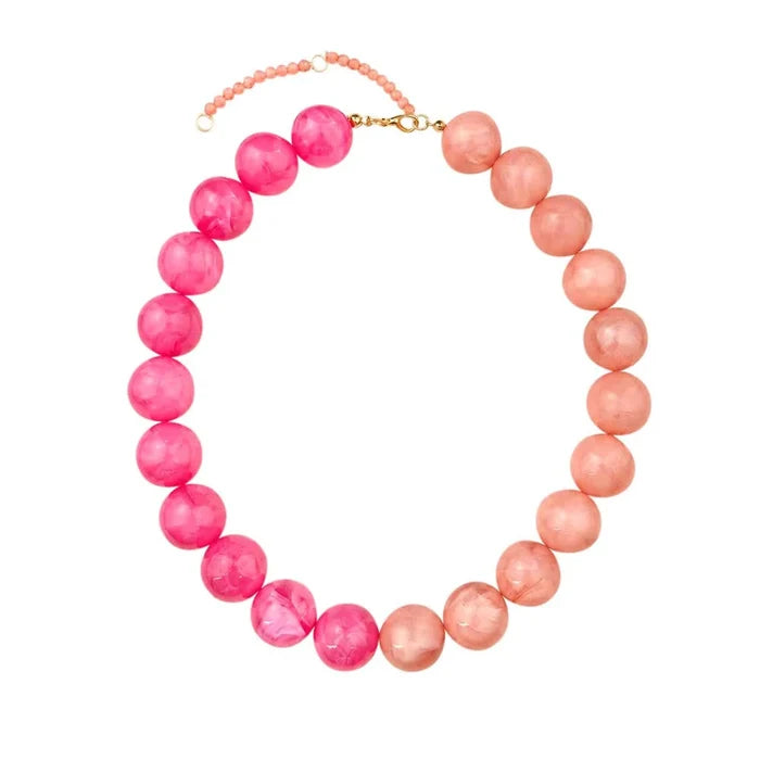 A beaded necklace featuring a color gradient from bright pink on one side to soft peach on the other, with a small gold clasp and extender chain, shown on a plain white background.