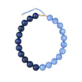 A beaded necklace featuring a gradient of blue beads, transitioning from deep navy on one side to light sky blue on the other, with a small gold clasp and extender chain at the top, shown on a plain white background.